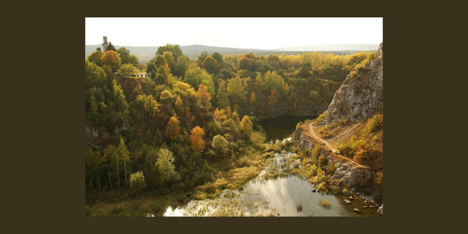 A scenic view of a lake nestled within a quarry surrounded by autumn trees with hints of orange and yellow foliage.